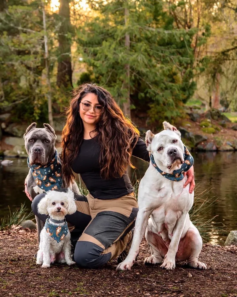 Marianna, founder of Amani K9, kneeling with three dogs by a pond