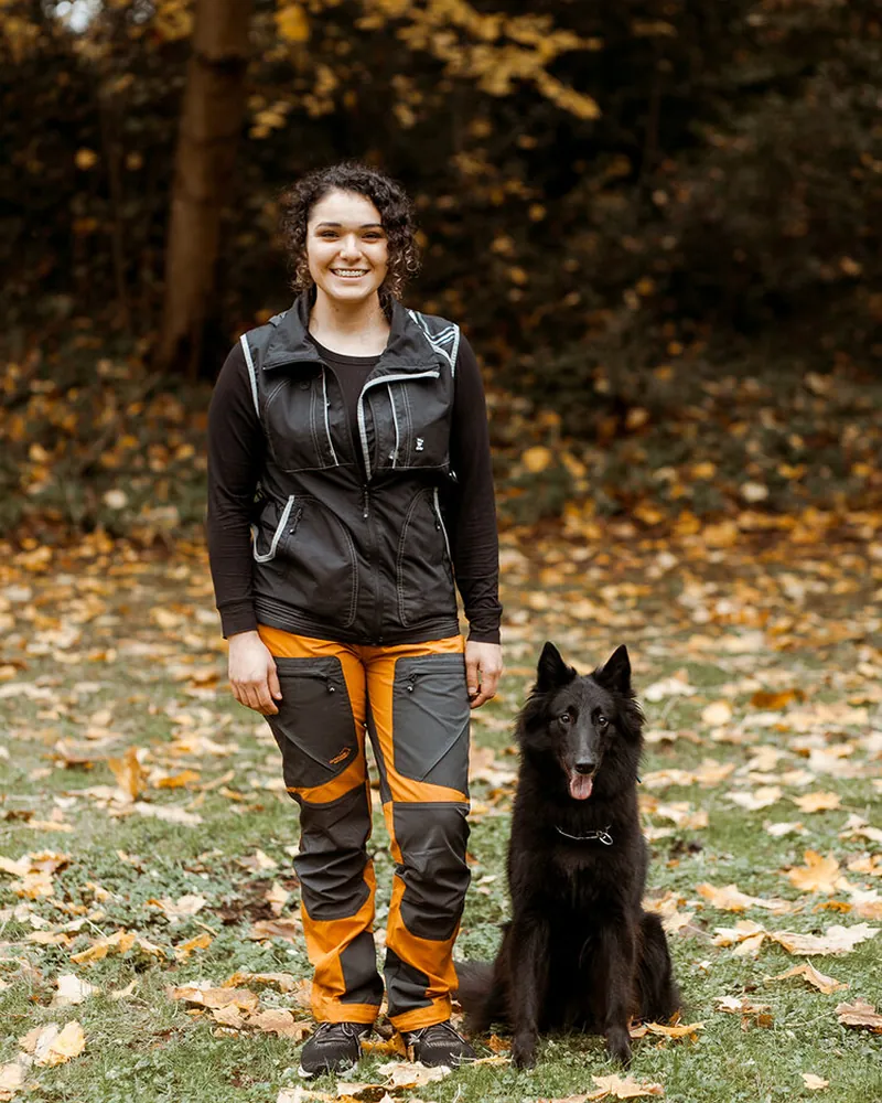 Niquolette, Amani K9 trainer, standing with a black shepherd in fall leaves